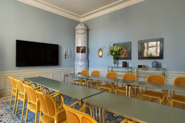 Elegant matsal med blå väggar, gula stolar, utsmyckad keramikhäll, stor TV och konstverk. Vita lister och dekorativa taklister.