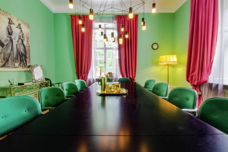 Livfull matsal med gröna väggar, rosa gardiner, svart bord, blågröna stolar, modern belysning och vintagekonst. Gyllene accenter överallt.